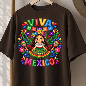 Pode incluir: Uma t-shirt castanho-escura com um gr&aacute;fico colorido de uma personagem de desenho animado com cabelo entran&ccedil;ado, uma coroa de flores e um vestido verde. A personagem est&aacute; rodeada de maracas, flores e folhagem. O texto VIVA MEXICO est&aacute; em negrito.
