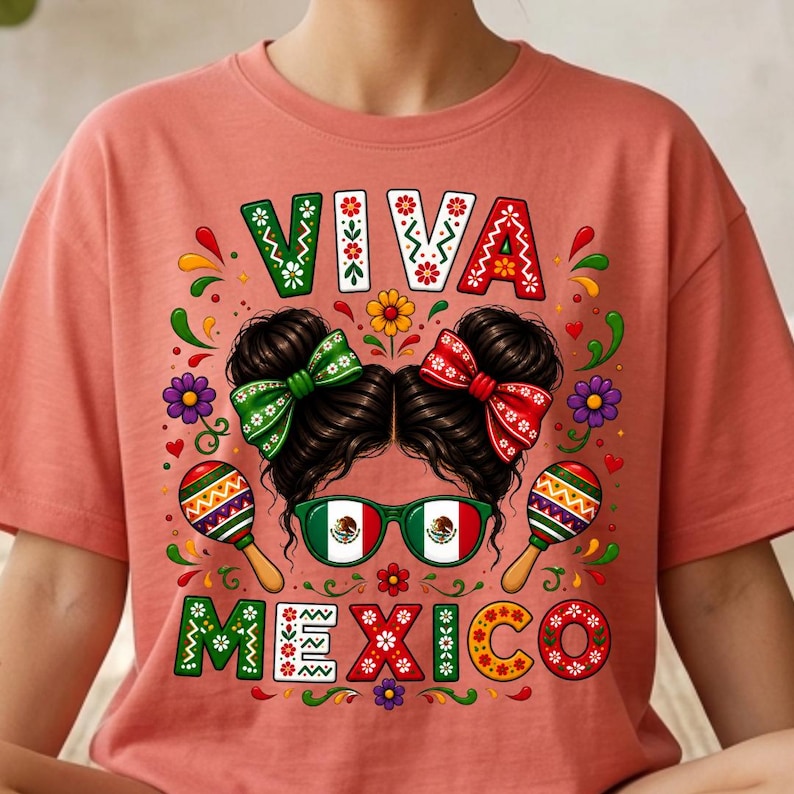 Pode incluir: Uma t-shirt cor de coral com uma impress&atilde;o gr&aacute;fica de cabelo escuro em dois coques com la&ccedil;os verdes e vermelhos, &oacute;culos de arma&ccedil;&atilde;o verde com a bandeira do M&eacute;xico e duas maracas. O texto VIVA MEXICO est&aacute; impresso em letras decorativas.