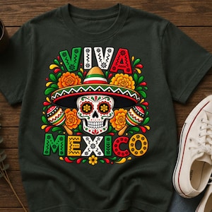 Pode incluir: Uma t-shirt cinzento-escura com uma impress&atilde;o gr&aacute;fica de uma caveira de a&ccedil;&uacute;car a usar um sombrero, ladeada por duas maracas e flores de cal&ecirc;ndula cor de laranja. O texto VIVA MEXICO est&aacute; impresso em letras arrojadas e coloridas.