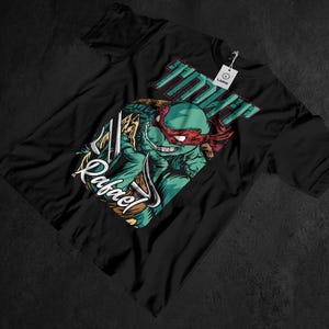 May include: Black t-shirt featuring a graphic of Raphael from Teenage Mutant Ninja Turtles. The design includes the word "Raphael" in a stylized font, and the word "TMNT" in green. The shirt has a "Large" tag.