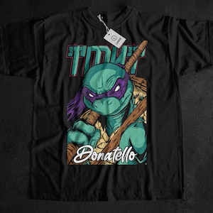 May include: Black t-shirt featuring a graphic of Donatello from the Teenage Mutant Ninja Turtles. The design includes a teal turtle with a purple mask, holding a bo staff. The word "Donatello" is written in a stylized font.
