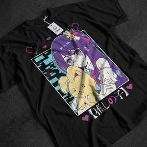 Może przedstawiać: Czarna koszulka z grafiką w stylu anime. Grafika przedstawia postać z fioletowymi włosami i żółtą zabawką. Projekt jest obramowany białą obwódką i japońskim tekstem. Różowe serca są rozrzucone wokół projektu.