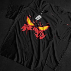 May include: Black t-shirt featuring a red and yellow graphic design of a stylized face with sharp features and intense eyes. The shirt has a tag that reads "LARGE". The design is centered on the front of the shirt.