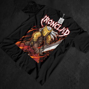 May include: Black t-shirt featuring a warrior illustration with a gold helmet and a sword, set against a fiery background. The word "IRONCLAD" is displayed in a stylized font above the warrior. A "LARGE" tag is attached.