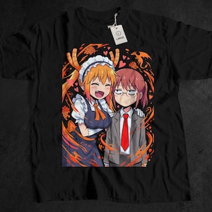 May include: Black t-shirt featuring a colorful anime-style illustration of two characters. One character is in a maid outfit with orange hair, and the other is in a gray suit with a red tie. The design includes orange and red accents.