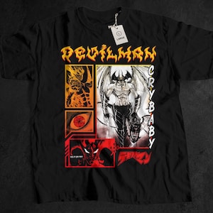 May include: Black t-shirt featuring a graphic design with the text "DEVILMAN CRYBABY" in yellow and white. The design includes illustrations of a winged demon, a fiery figure, and other graphic elements in red, orange, and white.