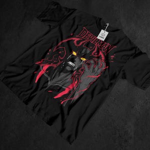 May include: Black t-shirt featuring a graphic of a crying demon with yellow eyes and red accents. The word "DEVILMAN" is printed in red across the top. A white tag with the word "LARGE" is attached to the shirt.