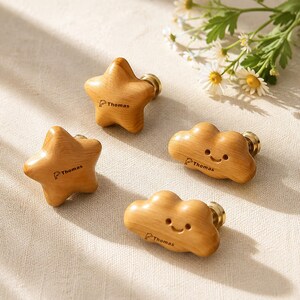 Puede incluir: Cuatro pomos de madera para muebles con acabado liso, que incluyen dos pomos en forma de estrella y dos en forma de nube con caras sonrientes. Cada pomo está grabado con un pequeño icono de delfín y el nombre Thomas sobre una base de metal dorado.