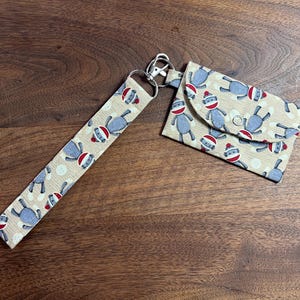 May include: A beige fabric wallet and matching lanyard with a repeating pattern of gray sock monkey illustrations wearing red and white striped hats. The wallet has a snap closure and a silver key ring.