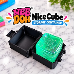 May include: A black plastic storage container with an open hinged lid. Inside the container sits a translucent green square Nee Doh Nice Cube with a marbled texture and the brand name embossed on the top surface. The text Nee Doh Nice Cube Storage Container is visible above the object.