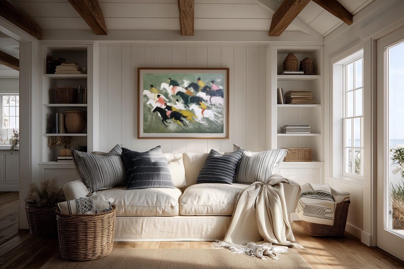 May include: A cozy living room scene featuring a cream-colored sofa with striped and solid pillows. A framed painting of horses racing hangs above the sofa. Wicker baskets and a neutral-toned rug complete the inviting space.