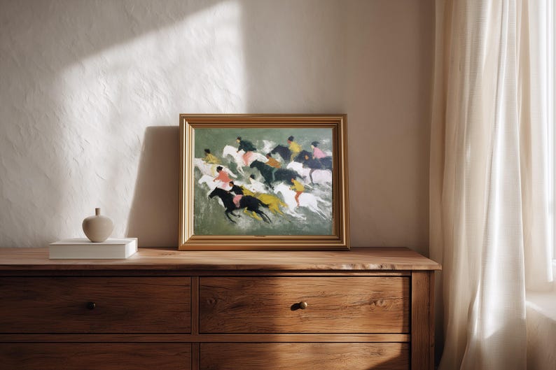 May include: A framed painting depicting a horse race with riders in various colors. The artwork is in a gold frame and rests on a wooden dresser. A small, beige decorative object sits on a white box to the left of the painting.