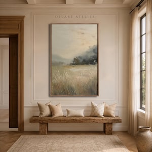 May include: A vertical rectangular framed landscape painting featuring a muted field of tall grasses in shades of beige, green, and grey under a soft, hazy sky. The text DELARÉ ATELIER is printed in small, dark letters above the artwork.