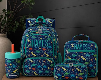 May include: A dark blue backpack, lunch bag, pencil case, and cup set featuring a colorful dinosaur pattern. The backpack and lunch bag are personalized with the name HAYES in large letters. The cup has a bright orange straw and lid.