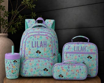 May include: A light blue backpack, lunch bag, pencil case, and tumbler set featuring a repeating mermaid pattern. The backpack and lunch bag are personalized with the name LILAH in purple text. The tumbler has a purple lid and straw.
