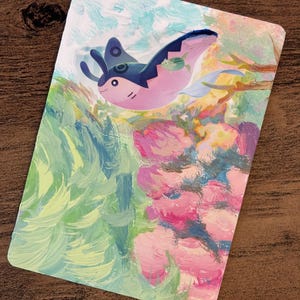 May include: A rectangular art print featuring a stylized illustration of a pink and blue manta ray-like creature with a small fish. The background has brushstrokes of green, blue, and pink, resembling an underwater scene.
