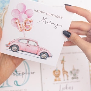 May include: A birthday card with a pink car, balloons, and the number 16. The card reads "Happy Birthday Milaya" in elegant script. The card is held by a person.