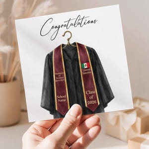 May include: A square card featuring a black graduation gown and a maroon stole hanging from a gold hanger. The text reads Congratulations, Bachelor of Science BIOLOGY, School Name, Lauren Sanchez, and Class of 2026, with a small Mexican flag icon.