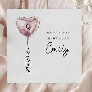 May include: A square birthday card with a heart-shaped pink balloon featuring the number 9. The card reads "Happy 9th Birthday Emily" in black script. The word "nine" is written in script below the balloon.