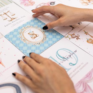 May include: A collection of greeting cards with various illustrations. One card features a teddy bear with a party hat, another has a gymnast, and others have animals. The cards are arranged on a white surface.
