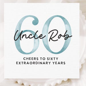 May include: A white square card with the text "60 Uncle Rob" in teal and black. The number 60 is in a teal watercolor style. Below the text is "Cheers to Sixty Extraordinary Years". The card is on a white plate.