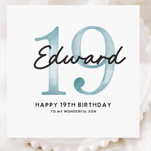 May include: A white square card with the number "19" in a teal watercolor style, the name "Edward" in black script, and the text "HAPPY 19TH BIRTHDAY TO MY WONDERFUL SON" in black. The card is on a white, scalloped-edge plate.