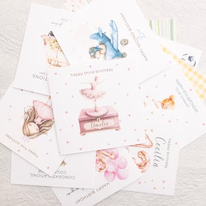 May include: A collection of watercolor birthday cards with various illustrations. Designs include a ballerina, a blue dragon, a girl with balloons, and a soccer ball. Each card has a unique message, such as "Happy 9th Birthday" and "Happy Second Birthday."