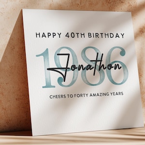 May include: A white card with the text "HAPPY 40TH BIRTHDAY" and "CHEERS TO FORTY AMAZING YEARS". The number "1986" is in teal, with the name "Jonathan" in a script font.