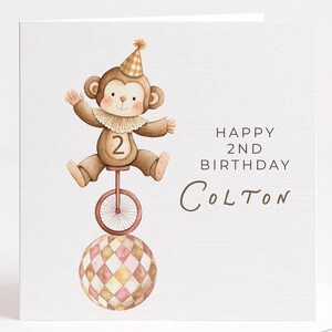 May include: A birthday card featuring a watercolor illustration of a monkey riding a unicycle on top of a patterned ball. The monkey wears a party hat and a ruffled collar. Text reads "Happy 2nd Birthday Colton."