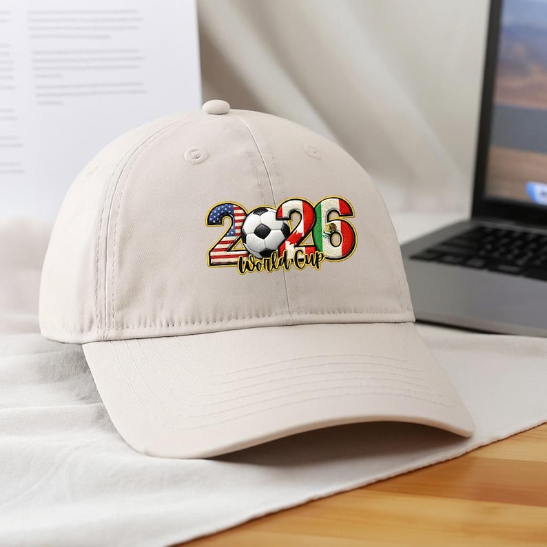 May include: A beige baseball cap featuring the text "2026 World Cup." The numbers are designed with the flags of the United States, Canada, and Mexico, with a soccer ball in the center.