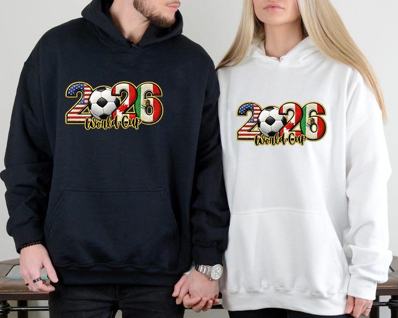 May include: Navy blue and white hooded sweatshirts with a graphic design for the 2026 World Cup. The design includes the number 2026, a soccer ball, and flags of the United States, Mexico, and Italy. The words "World Cup" are also included.