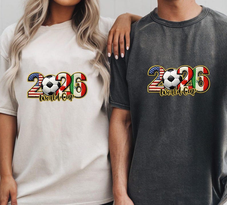 May include: Two t-shirts, one cream and one charcoal, featuring a graphic design for the 2026 World Cup. The design includes the number 2026 with the American and Mexican flags, a soccer ball, and the words "World Cup".