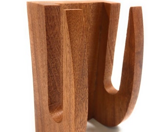 May include: A wooden stand with two U-shaped cutouts, designed to hold two items, such as mugs or glasses.