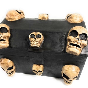 May include: A black wooden treasure chest with a skull design. The chest is decorated with eight small, carved skulls.