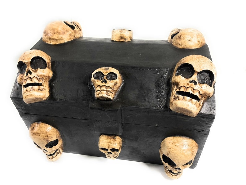 May include: A black wooden treasure chest with a skull design. The chest is decorated with eight small, carved skulls.