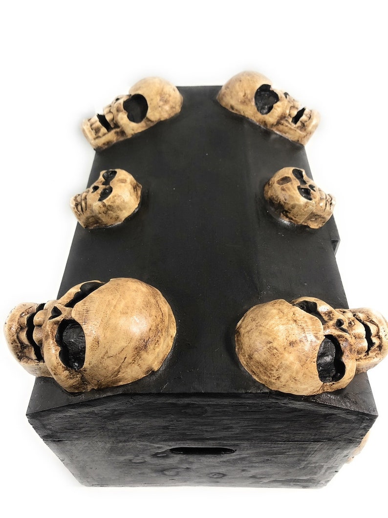 May include: A black wooden box with six skull-shaped accents. The box has a hinged lid and a small keyhole.