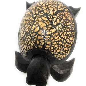 May include: A wooden turtle figurine with a black shell and a beige shell pattern. The turtle is carved with intricate details and has a smooth finish.