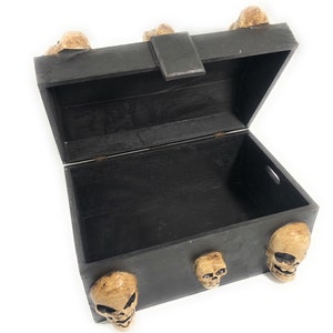 May include: A black wooden treasure chest with a hinged lid and skull accents. The chest is open and empty.