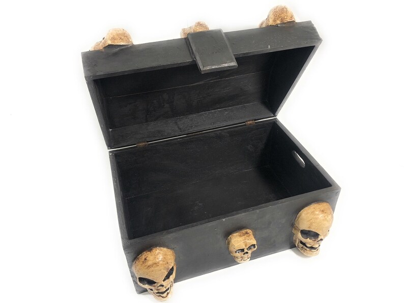 May include: A black wooden treasure chest with a hinged lid and skull accents. The chest is open and empty.