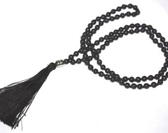 Puede incluir: Un collar de cuentas negras con un borla. Las cuentas son pequeñas y redondas, y la borla está hecha de hilo negro.