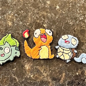 May include: Three embroidered patches featuring stylized cartoon creatures. The left patch is light green with a bulbous plant on its back. The center patch is orange with a flame on its tail. The right patch is light blue with a brown shell.