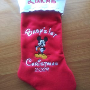 May include: Red Christmas stocking with white trim, embroidered with "Lukas", "Baby's 1st", Mickey Mouse, and "Christmas 2024".