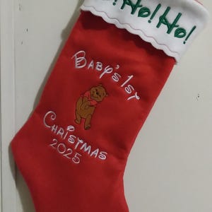 May include: Red Christmas stocking with white trim and embroidery. The stocking has the text "Ho! Ho! Ho!" on the cuff, "Baby's 1st Christmas 2025" on the stocking, and a cartoon bear.