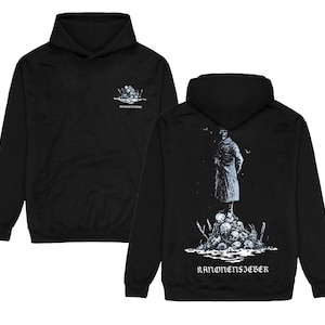 Op de afbeelding: Zwarte hoodie met een voorzak en capuchon. De voorkant heeft een kleine afbeelding van schedels en tekst. De achterkant toont een gedetailleerde illustratie van een figuur op een stapel schedels, met de tekst "KANONENSIEBER" eronder.