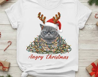 Puede incluir: Camiseta blanca con un gato gris gruñón con un gorro de Papá Noel y cuernos de reno, enredado en luces navideñas. El texto rojo debajo dice "Angry Christmas".