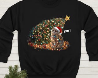 Puede incluir: Sudadera negra con un diseño navideño. Presenta un gato con gorro de Papá Noel frente a un árbol de Navidad decorado con luces de colores. El texto "WHAT?" es visible. Hay regalos en la base del árbol.