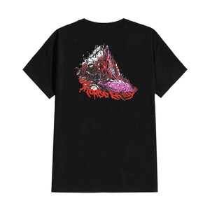 May include: Black t-shirt featuring a graphic design on the back. The design is a mix of red, pink, and white, depicting a creature with the text "TORSO REIFLE" in red. The shirt has short sleeves and a crew neck.