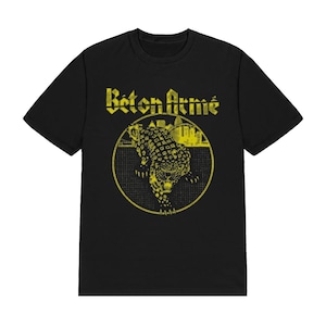 K&ouml;nnte beinhalten: Ein schwarzes Kurzarm-T-Shirt mit einem gelben Grafikdruck auf der Brust. Das Design zeigt den Schriftzug "B&eacute;ton Arm&eacute;" &uuml;ber einem kreisf&ouml;rmigen Emblem, das einen stilisierten Leoparden und eine Stadtsilhouette vor einem Rasterhintergrund enth&auml;lt.