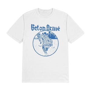 K&ouml;nnte beinhalten: Ein wei&szlig;es kurz&auml;rmeliges T-Shirt mit einem blauen Grafikdruck auf der Brust. Das Design zeigt den Schriftzug "B&eacute;ton Arm&eacute;" &uuml;ber einem kreisf&ouml;rmigen Emblem mit einem schleichenden Leoparden und einer Stadtsilhouette im Used-Look.