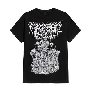 May include: Black t-shirt featuring a white graphic design. The design includes the text "Frozen Soul" in a stylized font above a detailed illustration of skeletons and skulls. The artwork is in a heavy metal style.